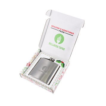 A stainless steel hip flask in a decorative gift box, featuring a logo and festive design elements. A stainless steel hip flask in a decorative gift box, featuring a logo and festive design elements.