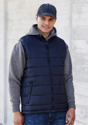 A man wearing a navy blue puffer vest over a grey hoodie, combined with denim jeans and a cap. The vest has a front zipper and pockets. A man wearing a navy blue puffer vest over a grey hoodie, combined with denim jeans and a cap. The vest has a front zipper and pockets.