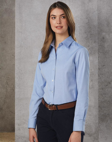 A light blue women's button-up shirt with long sleeves, featuring a collar and a logo, paired with dark trousers.