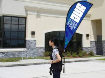 A person carrying a blue teardrop banner backpack with a logo outside a building.
