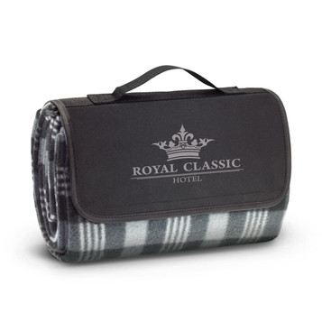A folded picnic blanket in grey and green plaid, featuring a black carrying strap and a logo on the front. A folded picnic blanket in grey and green plaid, featuring a black carrying strap and a logo on the front.