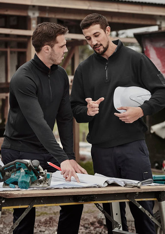 A black unisex Merino wool mid-layer pullover is worn by two men discussing plans at a construction site.