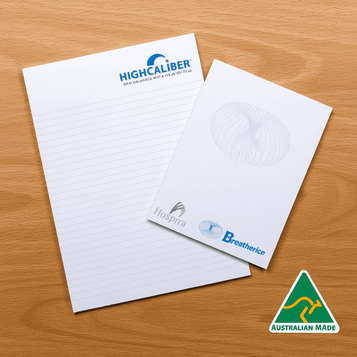 A notepad featuring lined pages, with a logo on the top and a smaller pad beside it, on a wooden surface. A notepad featuring lined pages, with a logo on the top and a smaller pad beside it, on a wooden surface.