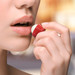 A red and white lip balm ball being applied to lips by a person with natural lips and soft focus background.