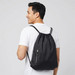 A man wearing a black drawstring bag with a logo on the back, featuring adjustable straps and a front zip pocket.