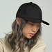 A black cap featuring a structured design and a curved brim, worn by a person with long, wavy hair.