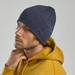 A navy blue beanie is worn by a person in a yellow hoodie, showcasing a textured pattern and a logo.