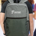 A grey and green backpack with a logo, featuring adjustable straps and a spacious front pocket.