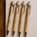 Four bamboo stylus pens with silver accents arranged on a light surface, each featuring a branding logo.
