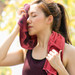 A woman wipes her forehead with a red cooling towel, showcasing its texture and functionality in an outdoor setting. A woman wipes her forehead with a red cooling towel, showcasing its texture and functionality in an outdoor setting.