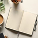 An open dark blue Moleskine 2027 planner with lined pages, surrounded by a coffee cup and stationery.