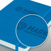 A blue notebook with a textured cover and an embossed logo. Features a ribbon bookmark and an elastic closure.