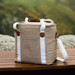 A tan canvas cooler bag with white straps and a brown handle, featuring a side pocket. A tan canvas cooler bag with white straps and a brown handle, featuring a side pocket.