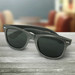 Carbon fibre sunglasses in grey, with dark lenses and a sleek design, displayed on a wooden surface. Carbon fibre sunglasses in grey, with dark lenses and a sleek design, displayed on a wooden surface.