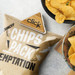 A bamboo handy clip secures a bag of chips, surrounded by crispy snacks on a textured surface.