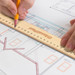 A wooden 30cm ruler rests on a blueprint with a hand holding a pencil. The ruler features a logo. A wooden 30cm ruler rests on a blueprint with a hand holding a pencil. The ruler features a logo.