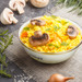 A Bendigo enamel bowl filled with yellow rice, mushrooms, and herbs, surrounded by fresh ingredients on a textured surface. A Bendigo enamel bowl filled with yellow rice, mushrooms, and herbs, surrounded by fresh ingredients on a textured surface.