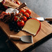 A wooden cheese board featuring cheese, cherry tomatoes, blueberries, and a set of metal cheese knives with wooden handles. A wooden cheese board featuring cheese, cherry tomatoes, blueberries, and a set of metal cheese knives with wooden handles.