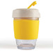 A reusable coffee cup in clear glass with a yellow silicone band and a light-colored lid. It features a logo. A reusable coffee cup in clear glass with a yellow silicone band and a light-colored lid. It features a logo.