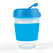 A reusable coffee cup in clear glass with a blue silicone lid and sleeve. It features a logo on the sleeve. A reusable coffee cup in clear glass with a blue silicone lid and sleeve. It features a logo on the sleeve.