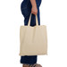A beige reusable calico bag with short handles, held by a person in blue jeans. A beige reusable calico bag with short handles, held by a person in blue jeans.