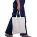 A white cotton tote bag with short handles, being held by a person wearing blue jeans. A white cotton tote bag with short handles, being held by a person wearing blue jeans.