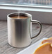 A stainless steel coffee mug with steam rising from the hot beverage inside, positioned near a plate of pancakes. A stainless steel coffee mug with steam rising from the hot beverage inside, positioned near a plate of pancakes.