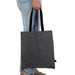 A grey felt tote bag with black handles is held by a person wearing jeans. The bag features a logo. A grey felt tote bag with black handles is held by a person wearing jeans. The bag features a logo.