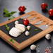 A bamboo cheese board featuring a black slate surface, sliced mozzarella, cherry tomatoes, and cheese knives. A bamboo cheese board featuring a black slate surface, sliced mozzarella, cherry tomatoes, and cheese knives.