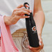 A drink bottle with a matte black finish, featuring a logo, held by a person wearing light-coloured clothing. A drink bottle with a matte black finish, featuring a logo, held by a person wearing light-coloured clothing.