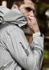 A reflective grey waterproof jacket with a logo, featuring a close-up of a model wearing it. A reflective grey waterproof jacket with a logo, featuring a close-up of a model wearing it.