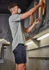 A man wearing a light grey t-shirt and dark shorts adjusts materials on a wall in a workshop setting.