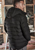 A black unisex hooded puffer jacket with a quilted design, worn by a person from a side angle.