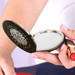 A compact mirror with a circular design, featuring a reflective surface and a dark exterior, held in a hand. A compact mirror with a circular design, featuring a reflective surface and a dark exterior, held in a hand.