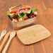 A metal lunch box filled with a sandwich, lettuce, strawberries, and a cutting board made of wood beside it. A metal lunch box filled with a sandwich, lettuce, strawberries, and a cutting board made of wood beside it.