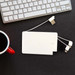 A white 5,000mAh power bank with built-in charging cables, placed on a dark surface near a keyboard and a mug. A white 5,000mAh power bank with built-in charging cables, placed on a dark surface near a keyboard and a mug.