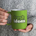 A coffee mug featuring the text "fresh Ideas" in a bold, playful font, set against a vibrant green background.