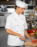 A chef wearing a white Chef's Cap and uniform, chopping vegetables in a kitchen setting.