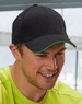 A black cap with a green peak, featuring a logo, worn by a smiling man in a bright yellow shirt.