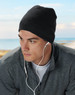 Acrylic knitted marl beanie in dark grey worn by a model with earbuds, set against a coastal background.
