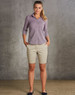 A model wearing khaki chino shorts paired with a button-up shirt, standing against a textured grey background.