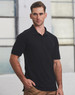 A man in a black polo shirt stands against an industrial background, featuring short sleeves and a standard collar.