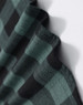 A close-up of a unisex flannel shirt in black and green plaid fabric, featuring a logo.