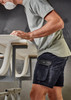A man wearing navy rugged cooling stretch shorts and a grey t-shirt, working at a table with a surfboard. A man wearing navy rugged cooling stretch shorts and a grey t-shirt, working at a table with a surfboard.
