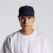 A navy trucker cap featuring a mesh back and a solid front, worn by a person in a white t-shirt.