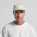 A light beige cap with a structured five-panel design, worn by a model in a plain white t-shirt. A light beige cap with a structured five-panel design, worn by a model in a plain white t-shirt.