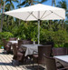 A white market umbrella without a valance positioned over outdoor tables and chairs surrounded by lush greenery. A white market umbrella without a valance positioned over outdoor tables and chairs surrounded by lush greenery.