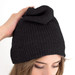 A black beanie with a unique fold at the top, held by a person's hand. It features a logo. A black beanie with a unique fold at the top, held by a person's hand. It features a logo.