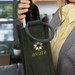 A drink bottle carrier in green jute with a decorative logo, held by a person in a grey blazer. A drink bottle carrier in green jute with a decorative logo, held by a person in a grey blazer.