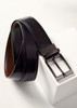 A men's leather reversible belt featuring black on one side and brown on the other, with a metallic buckle and branding. A men's leather reversible belt featuring black on one side and brown on the other, with a metallic buckle and branding.